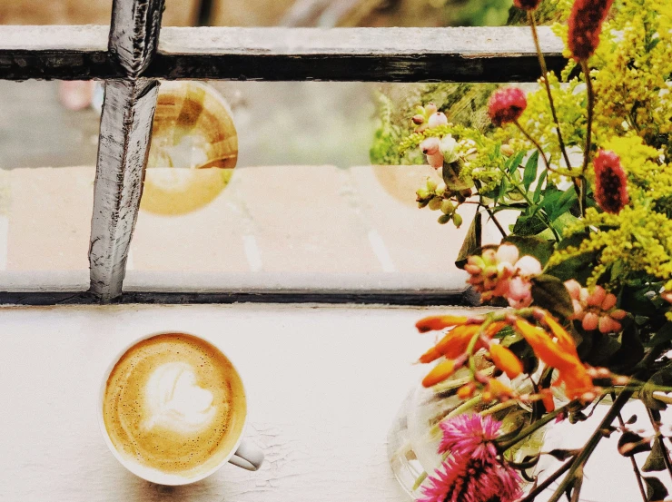 a coffee cup sits on a window sill near some flowers