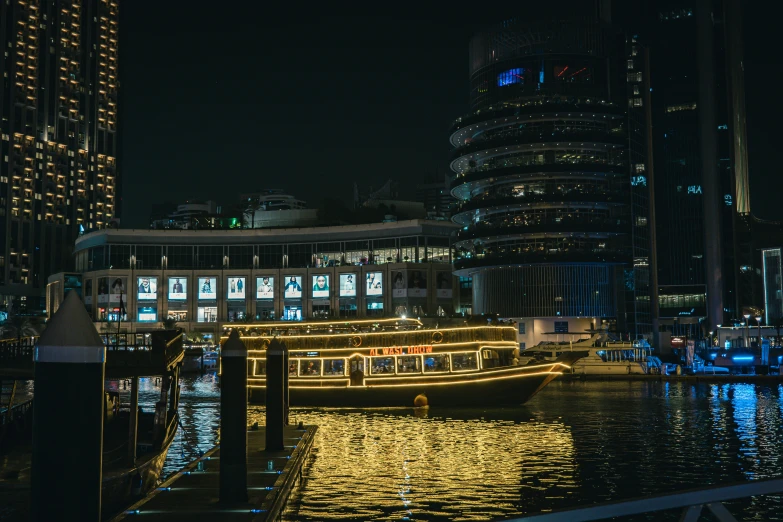 an illuminated boat on the river in front of some high rise buildings