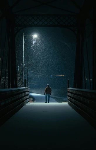 a man walks down the street under an overhead bridge at night