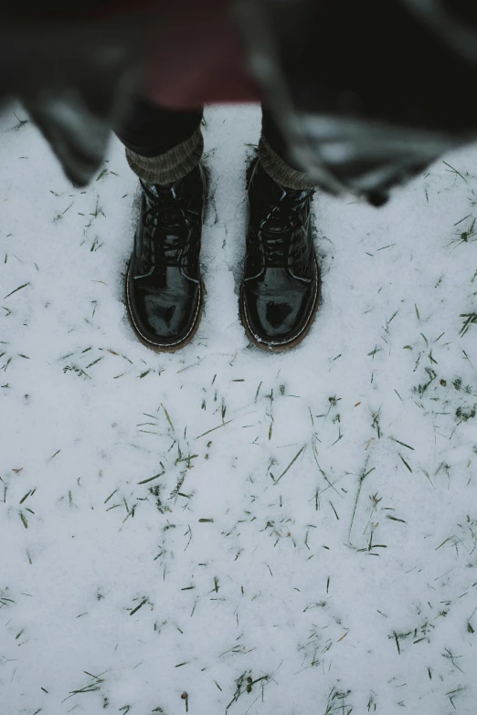 a person's feet in a pair of black boots on white snow