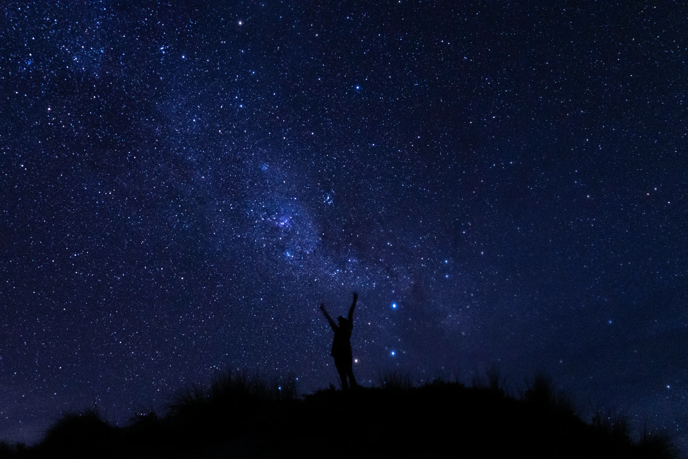 someone stands on a hill at night and stars above