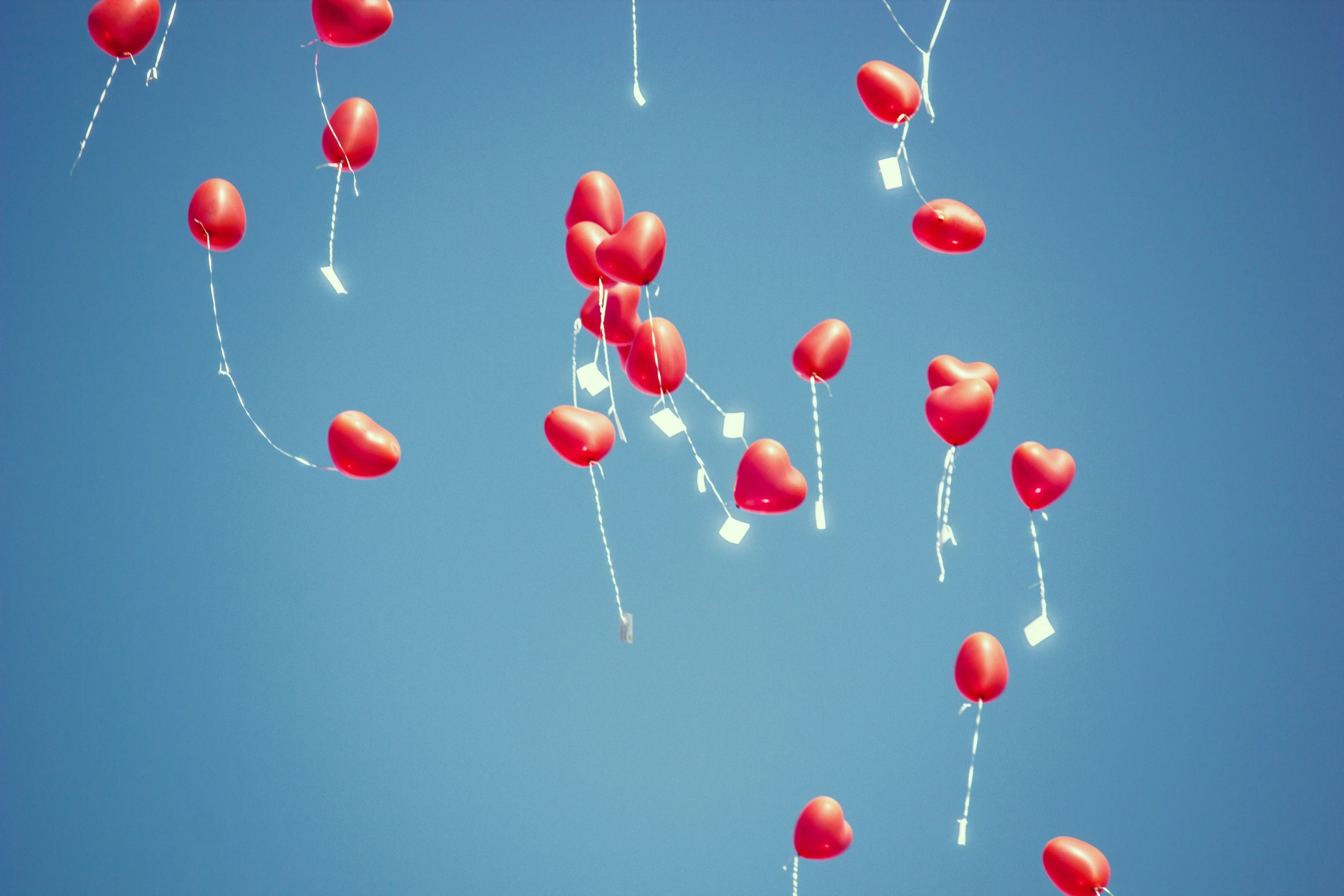 several red balloons are floating up in the air