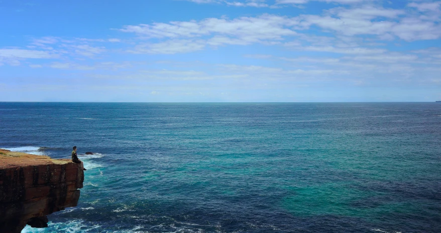 a person is standing on the cliff looking out to sea