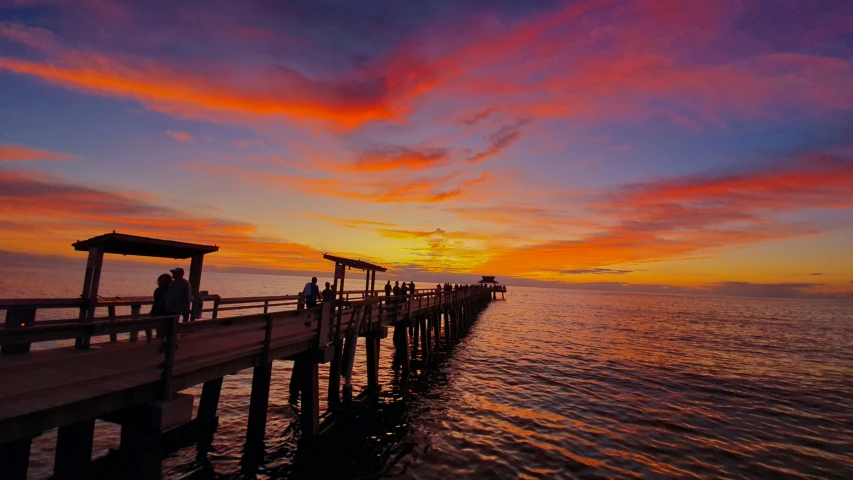 colorful clouds over ocean as people stand on wooden pier
