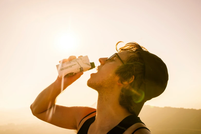 a man drinks from a bottle while standing on a hill