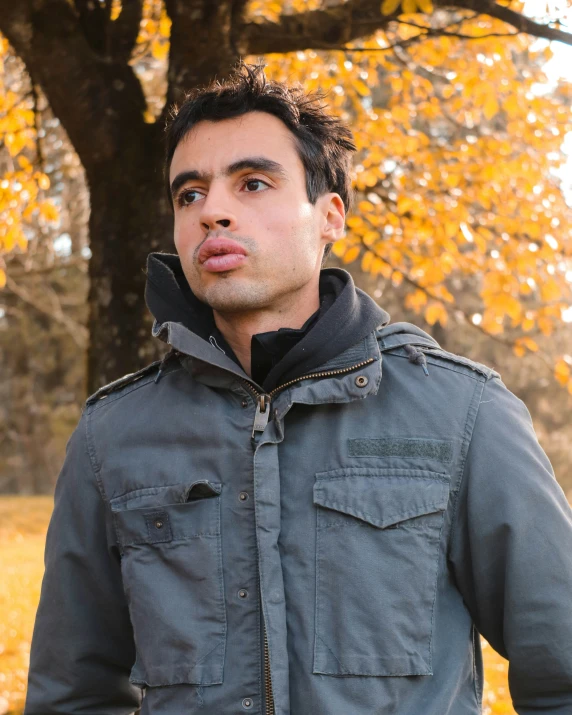 a man with a goofy look standing in front of trees