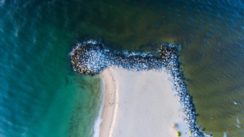 aerial view of beach and water, with jetty in the foreground