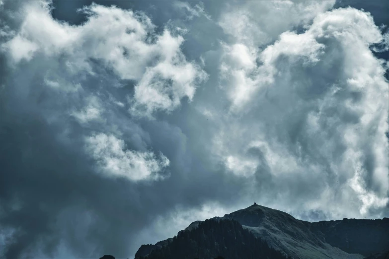 a cloudy sky above some mountains with a bird on top