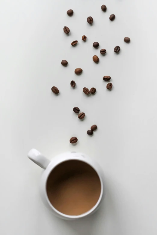 coffee beans fall into the white cup of coffee