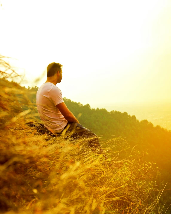 a man sits on a mountain top in front of the sun
