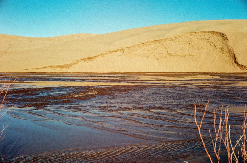 the landscape shows sandy dunes against the backdrop of blue skies and distant mountains