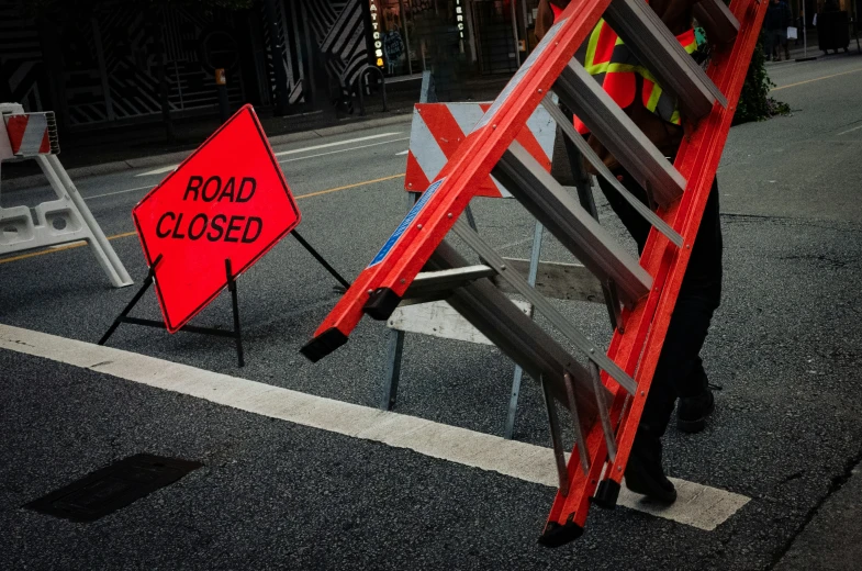 an open red ladder next to a road closed sign