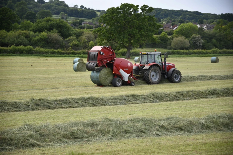 a farm worker riding a tractor with bales of hay