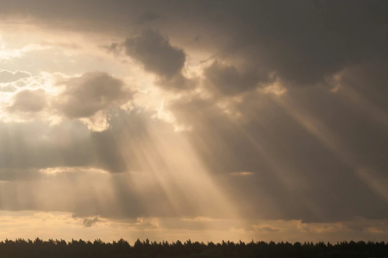 sun rays shining through the clouds above trees in a field