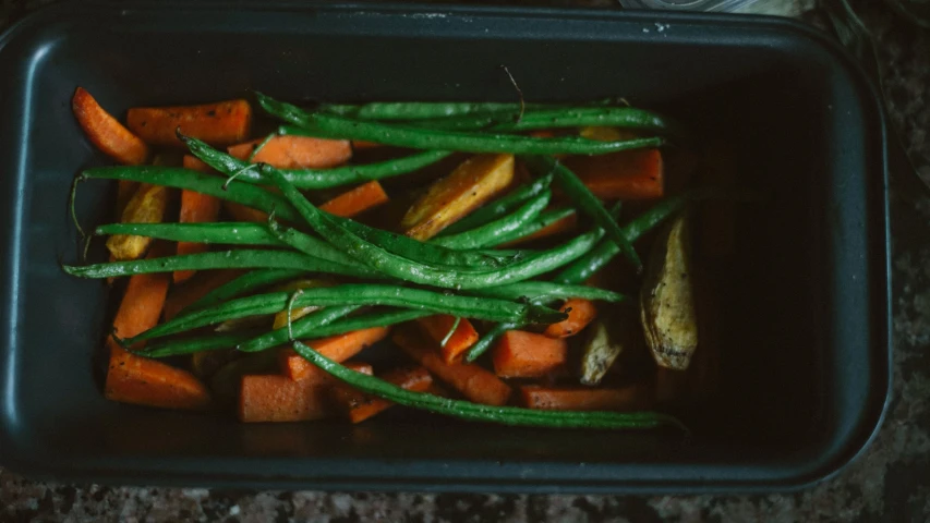 there is a black container filled with carrots and green beans