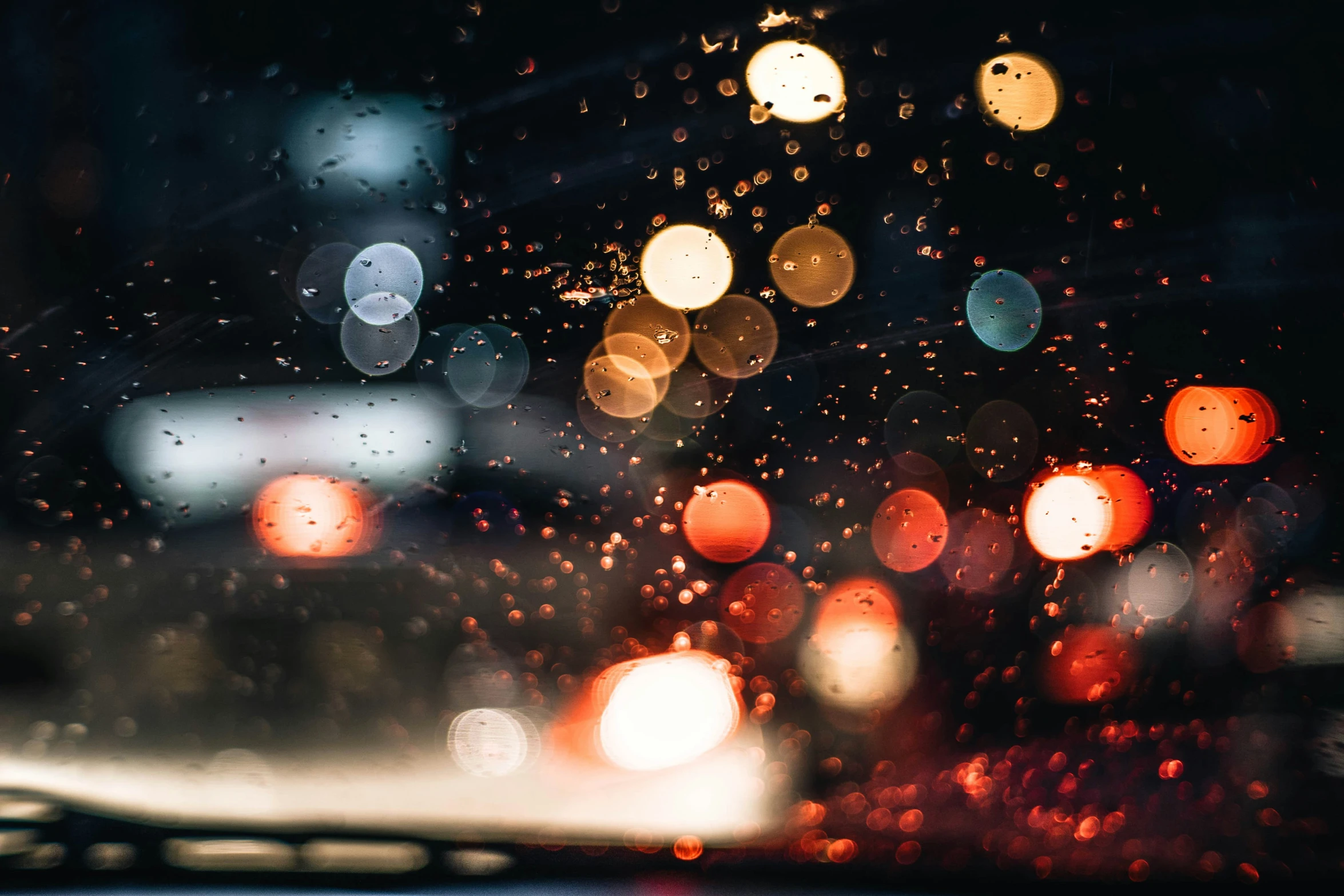 some lights on a rain soaked windshield as cars drive by