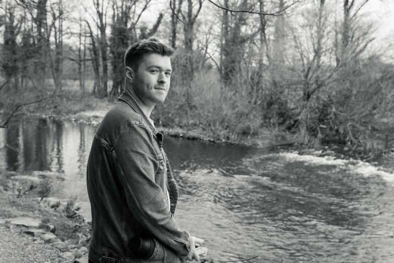 black and white pograph of a man sitting on a rock near water