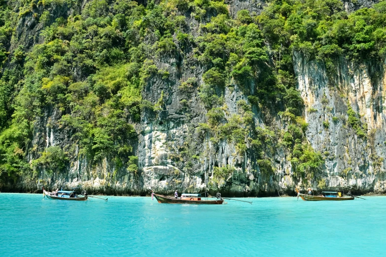 several boats are anchored in blue water between two cliffs