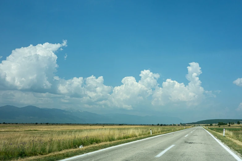 the road with blue sky and white clouds passes over a field