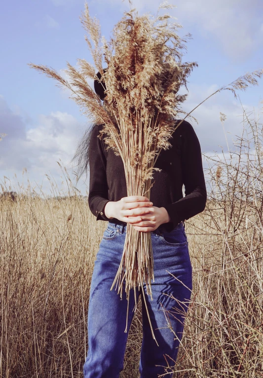 a woman standing in a wheat field holding some straws