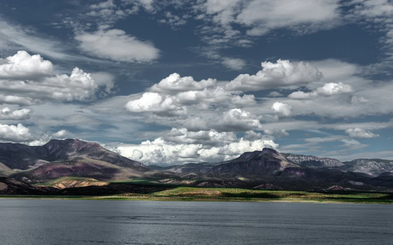 a lake with clouds, mountains and a boat floating on the water