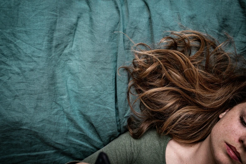 the girl has red hair, wearing an orange shirt and is laying down with her eyes closed