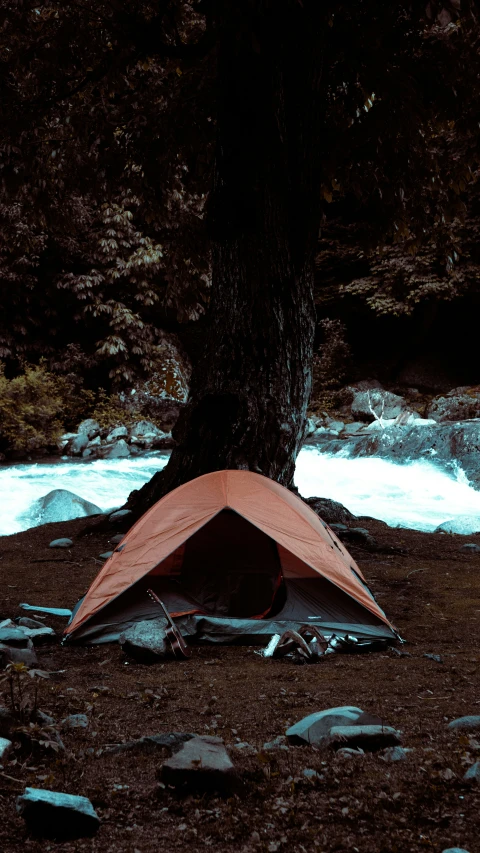 an orange tent next to a creek on rocky ground