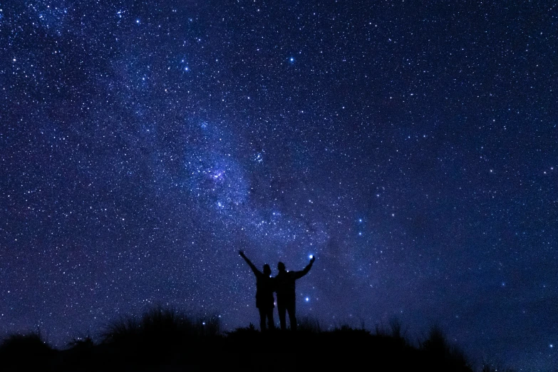 two people standing on top of a hill under stars