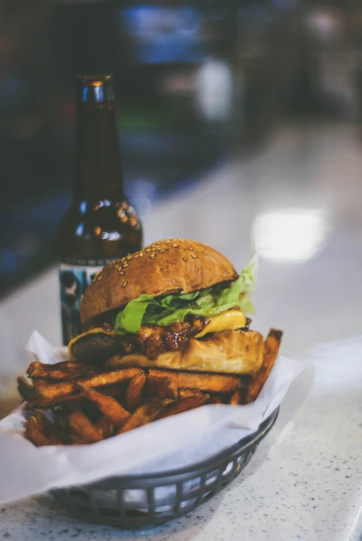 a burger is in a basket with fries next to a bottle of beer