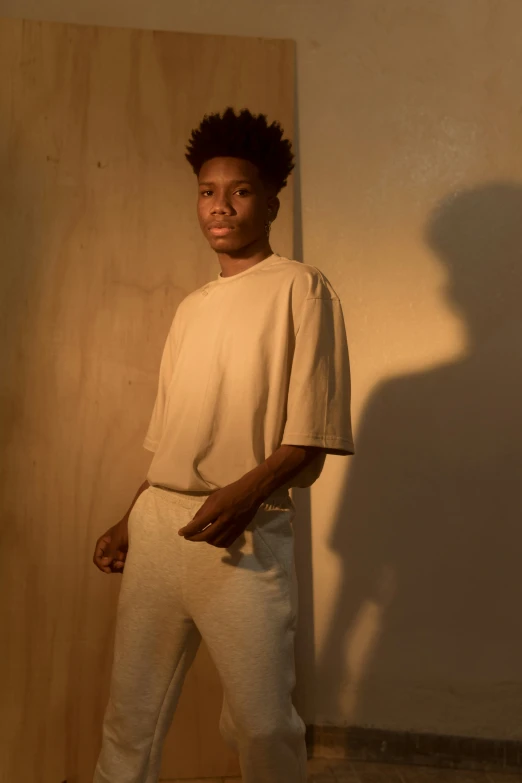 a young man standing next to a wall with his hands in his pockets