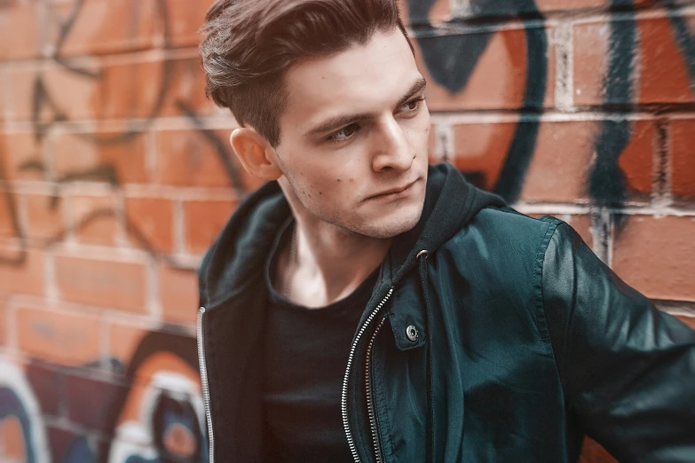 a young man with a black jacket in front of graffiti wall