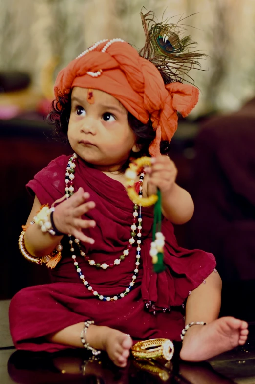 a baby wearing a red turban holds a small fan