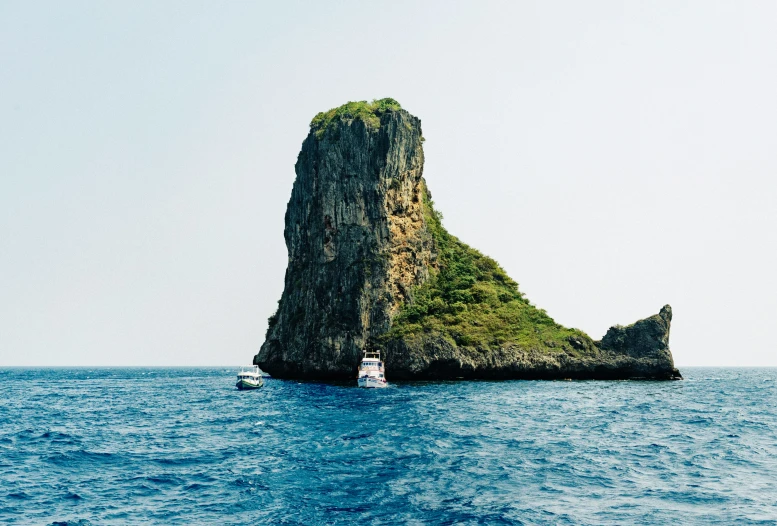 a small boat in the ocean near a tall rock