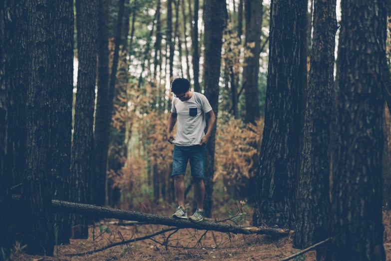 a man standing in the middle of the woods on a log