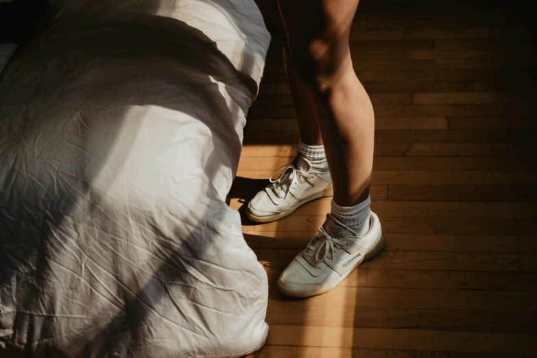 the foot of a person in white sneakers standing on a bed