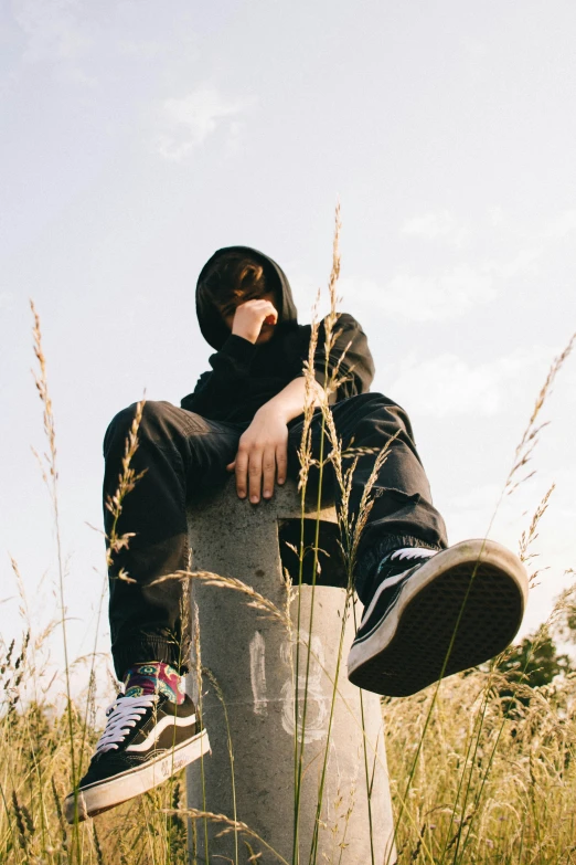 a boy that is sitting on a pillar in the grass