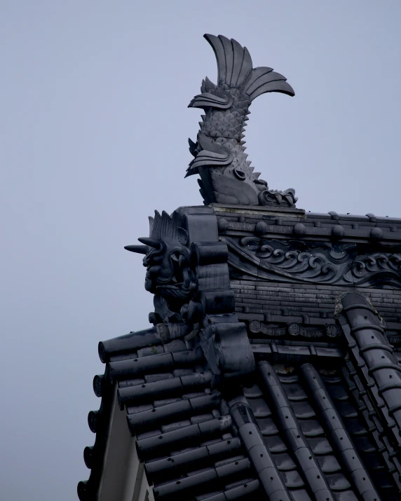 a grey brick building with an elaborate stone and metal bird on top