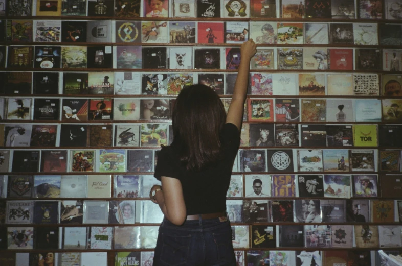 a woman in black shirt reaching up at album wall