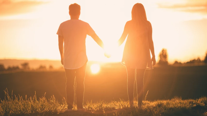 a couple holding hands while standing in a field at sunset