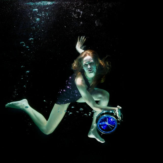 woman dressed as a mermaid floating underwater holding a clock