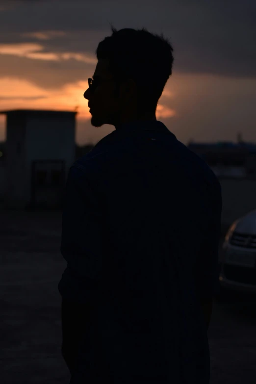 a man is standing in the parking lot while the sun sets