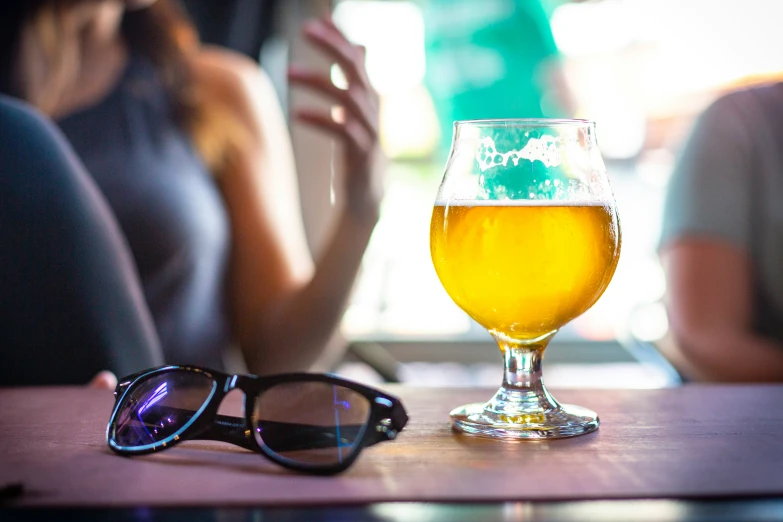 a glass of beer sits on the table with other people sitting at a bar in the background