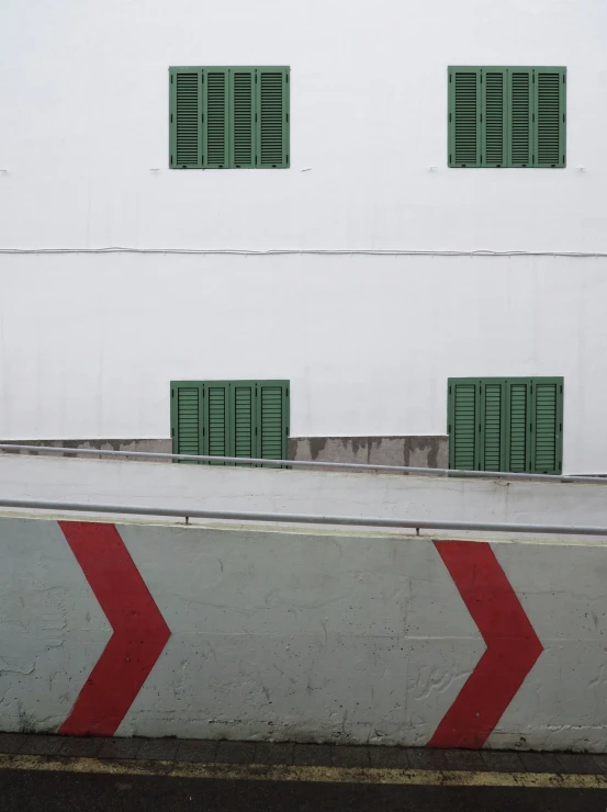a red and white wall some windows a red arrow and green shutters