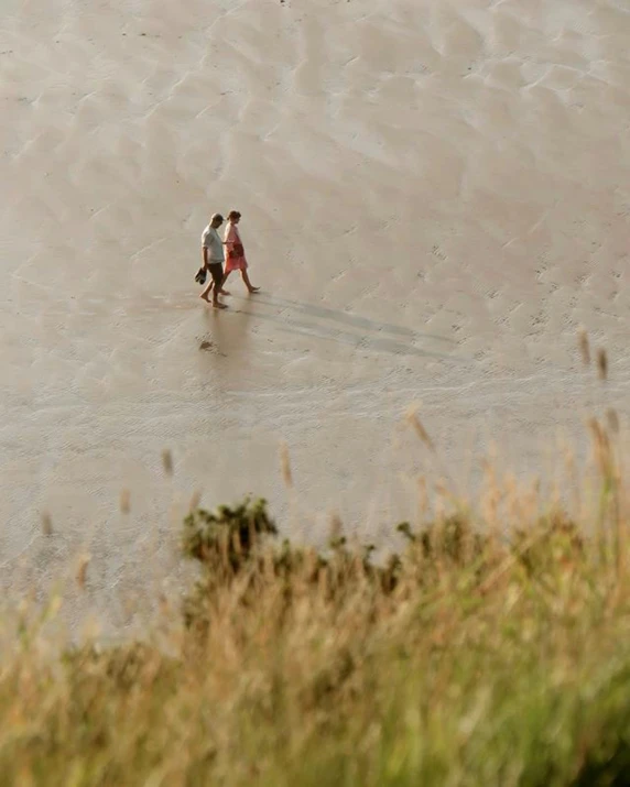 two people on a beach with one in the water walking the other in the sand