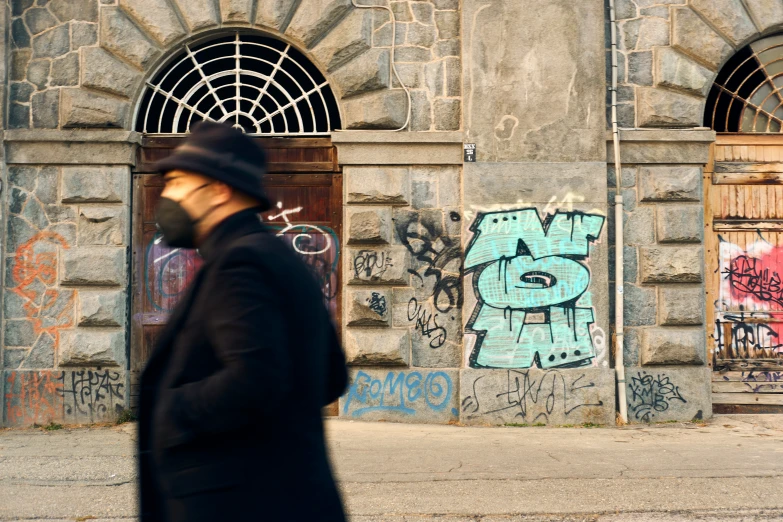 a man walking down a sidewalk past a door covered in graffiti