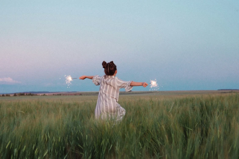 a woman standing in a field holding sparklers