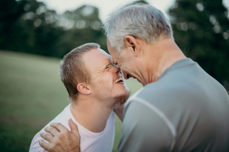 two men, one of which has his face close to each other, laugh while outside