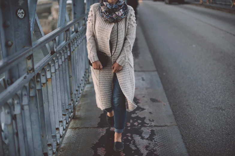 a woman is standing on a bridge wearing a scarf and coat