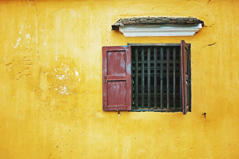 an open window with bars on a yellow painted building