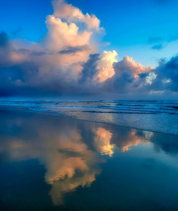 clouds are reflected in the wet sandy shore of the beach